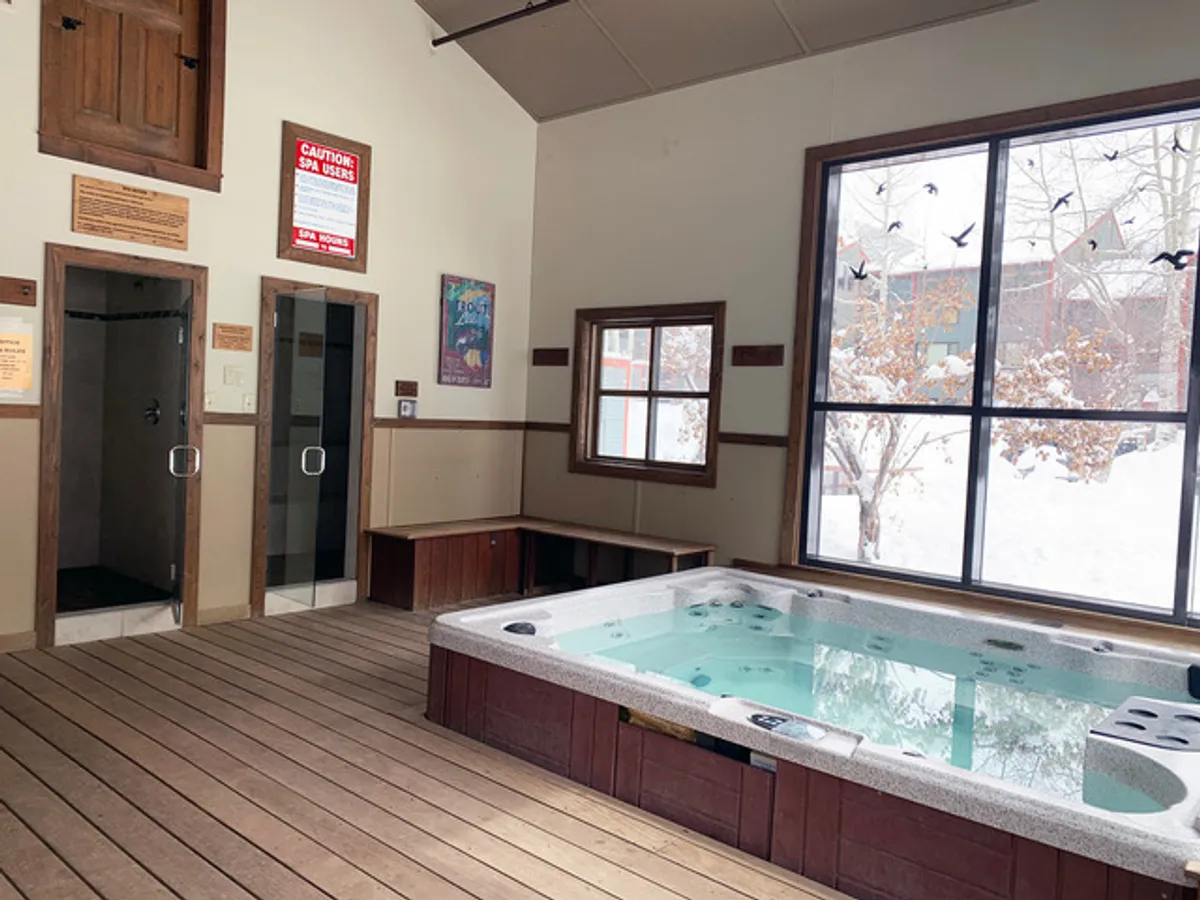 This image showcases a tranquil hot tub area with large windows, a wooden bench, and adjacent shower stalls, creating a peaceful spa-like retreat indoors. Soft light filters through the windows, and the space feels inviting and serene.