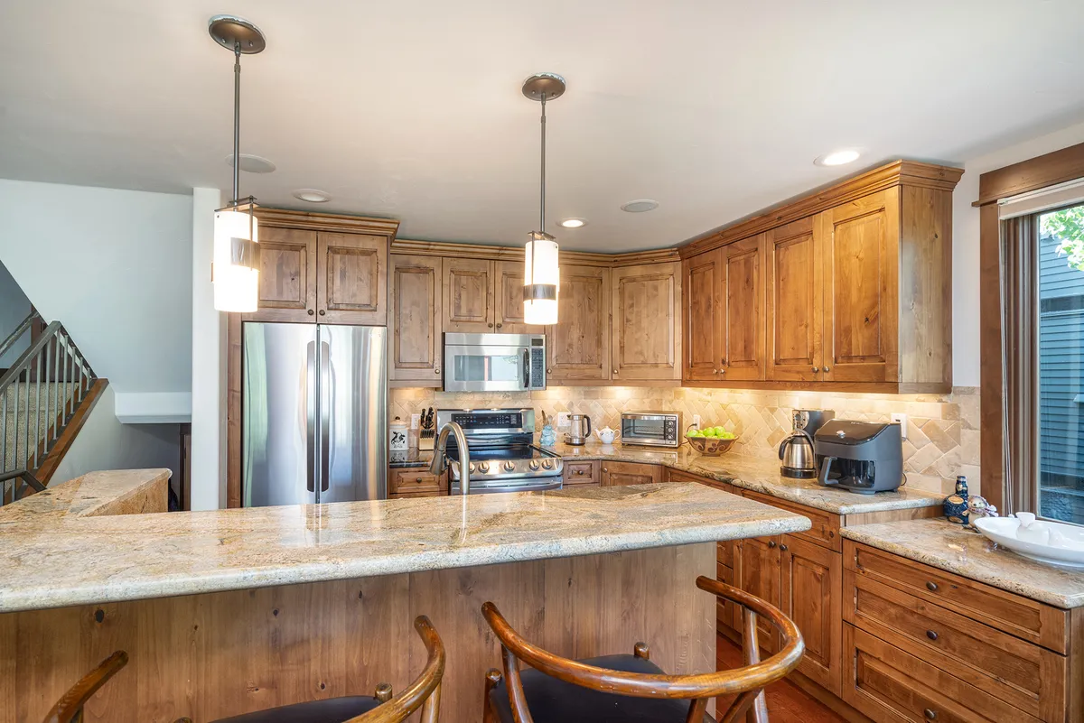 Another angle of the kitchen, highlighting the granite countertops, wooden cabinetry, and sleek stainless steel appliances. Pendant lighting and the open layout encourage a sense of connection between the kitchen, dining, and living areas—ideal for both casual breakfasts and festive family dinners.